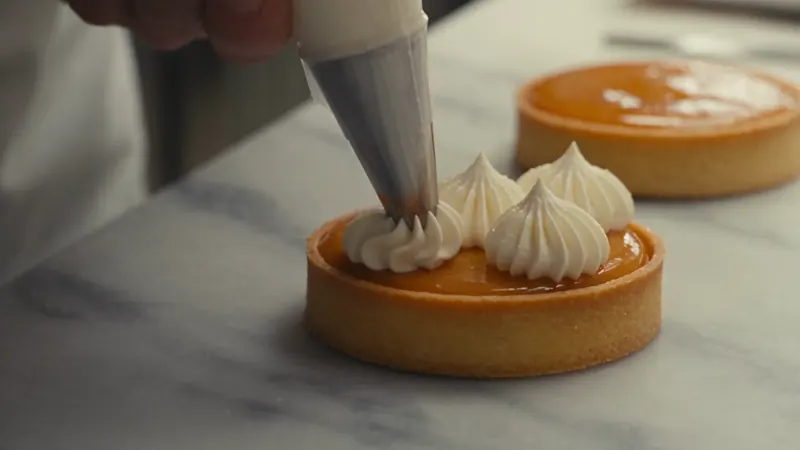 Gros plan : une poche à douille dépose une meringue sur une tarte